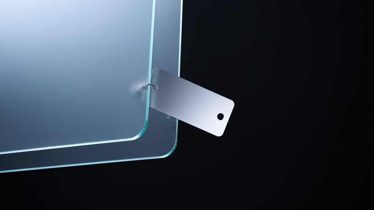 A brushed silver price tag floating beside layered panes of glass on a near-black studio background.