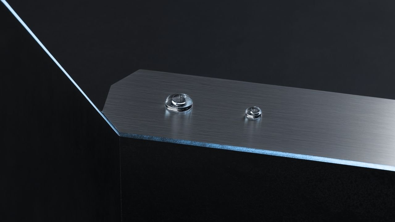 A brushed-silver balance scale with glass weights on a dark graphite surface, lit by cool ice-blue light.